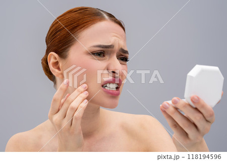 Upset beautiful girl inspecting skin problems in mirror Upset beautiful girl inspecting skin problems in mirror 118194596