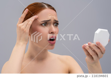 Attractive shocked young red-haired woman examining her pimples in mirror Attractive shocked young red-haired woman examining her pimples in mirror 118194601