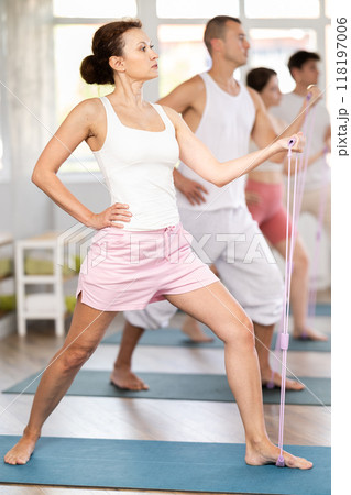 Happy young active woman with group people in sportswear, standing and training exercise with resistance bands in gym 118197006