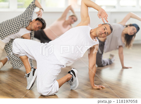 Man and his students perform hip hop dance on one bent leg, movement in horizontal plane near floor Man and his students perform hip hop dance on one bent leg, movement in horizontal plane near floor 118197058