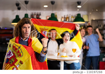 Group of sports supporters cheering for favorite team with flag of Spain while watching match game on TV in bar 118197288