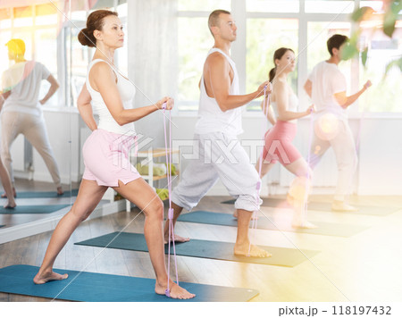 Young men and women doing shoulder workout with resistance band in standing positions Young men and women doing shoulder workout with resistance band in standing positions 118197432