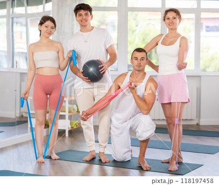 Young men and women posing together in training room holding resistance bands and pilates ball Young men and women posing together in training room holding resistance bands and pilates ball 118197458