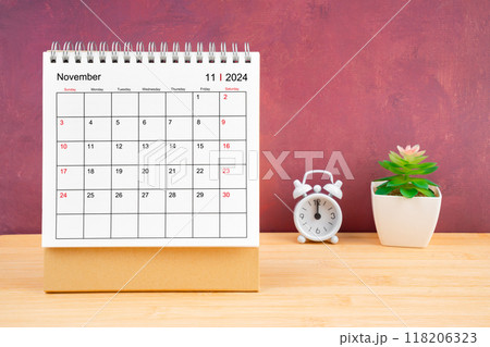 November Monthly desk calendar for 2024 year and alarm clock on wooden table. 118206323