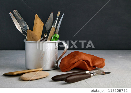 Many stacks and sculpting tools in a metal mug and pieces of clay and plasticine on a concrete table in a sculptor's workshop 118206752