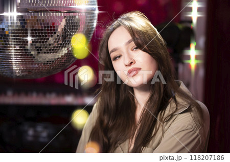Beautiful thoughtful girl in a nightclub against the background of bokeh and a disco ball. Beautiful thoughtful girl in a nightclub against the background of bokeh and a disco ball. 118207186