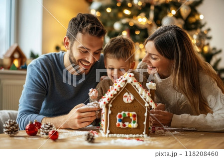 Family Decorating Gingerbread House with Christmas Tree in Background 118208460