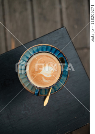 Top view of blue latte coffee cup with natural art. Hot coffee latte with latte art milk foam in blue cup mug on wood desk in a coffee shop at the cafe. Top view of blue latte coffee cup with natural art. Hot coffee latte with latte art milk foam in blue cup mug on wood desk in a coffee shop at the cafe. 118209271