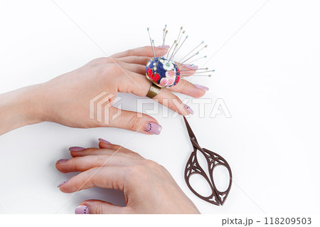 a ring with a small pillow for needles on a hand and scissors on a white background 118209503