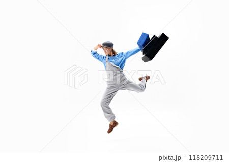 Energetic and free. Young, in retro attire soaring high with shopping bags, making shopping look like art against white background. Energetic and free. Young, in retro attire soaring high with shopping bags, making shopping look like art against white background. 118209711