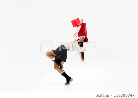 Young woman in dynamic pose, playfully swinging her shopping bags as she expresses her happiness against white studio background. Young woman in dynamic pose, playfully swinging her shopping bags as she expresses her happiness against white studio background. 118209747