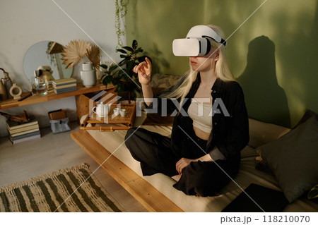 High angle of young woman with albinism wearing headset sitting on couch with legs crossed using virtual reality app High angle of young woman with albinism wearing headset sitting on couch with legs crossed using virtual reality app 118210070
