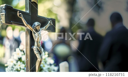 Mourners gather in the background of a cemetery, with a crucifix standing in the foreground 118210731