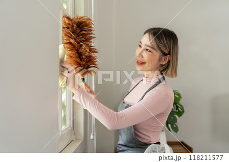 Housekeeper dusting window with feather duster in living room Housekeeper dusting window with feather duster in living room 118211577
