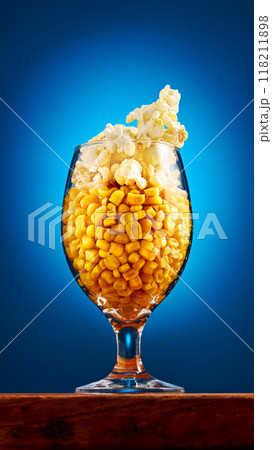 Beer glass filled with corn kernels and pop corn stands on table against blue studio background. Snacks and drinks for relax. Beer glass filled with corn kernels and pop corn stands on table against blue studio background. Snacks and drinks for relax. 118211898
