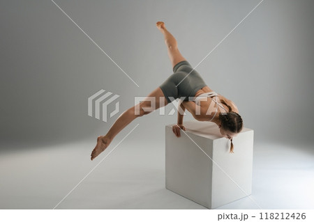Dancer performing an elegant pose on a white cube in a studio setting 118212426