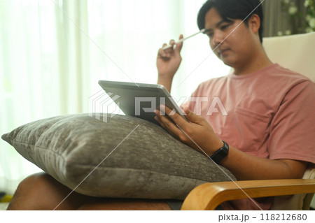 Concentrated male freelancer sitting on armchair and working with digital tablet at home 118212680