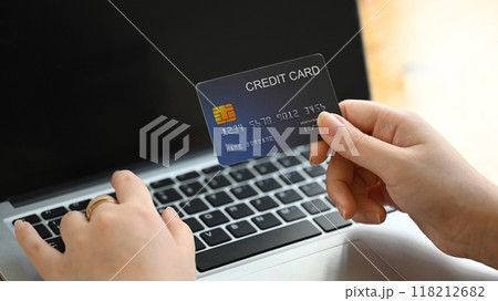 Close up of a person holding a credit card in front of a laptop, making online transaction Close up of a person holding a credit card in front of a laptop, making online transaction 118212682