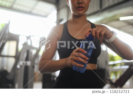 Sporty young woman drinking water while resting after exercising at health club 118212721
