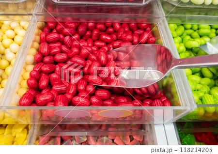 Red hard candies in plastic container with metal scoop. Close-up shot of candy display Red hard candies in plastic container with metal scoop. Close-up shot of candy display 118214205