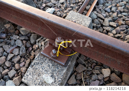 Close-up of a rusty railway track with a yellow ribbon tied around a bolt. Close-up of a rusty railway track with a yellow ribbon tied around a bolt. 118214218