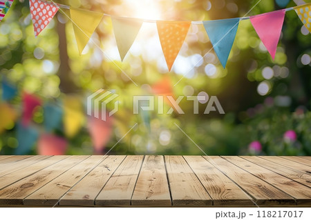 Wooden table desk surface for product display on a blurred festive background with colorful flags, park green leaves bokeh. Outdoor decorated for a festive celebration, garden picnic. Party banner 118217017