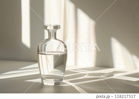 Elegant glass bottle with water casting soft shadows in filtered sunlight 118217317