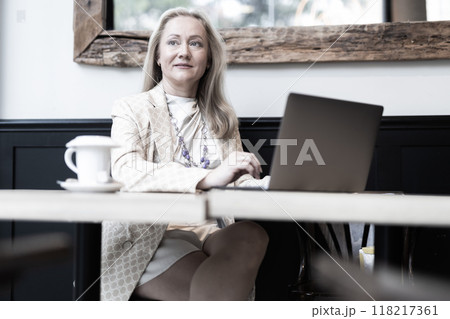 Positive woman using laptop and drinking coffee in cafe Positive woman using laptop and drinking coffee in cafe 118217361