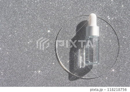 Transparent serum bottle with dropper on sparkling silver surface highlighting Transparent serum bottle with dropper on sparkling silver surface highlighting 118218756