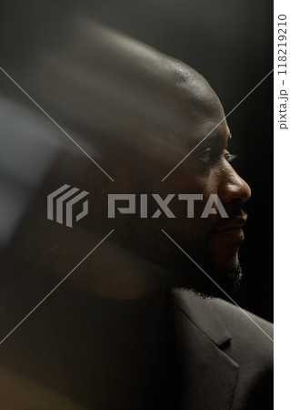 Vertical profile shot of adult African American man in formal suit looking away with expression of grief and sad contemplation lost in memories in low key lighted studio, ghost glare effect Vertical profile shot of adult African American man in formal suit looking away with expression of grief and sad contemplation lost in memories in low key lighted studio, ghost glare effect 118219210