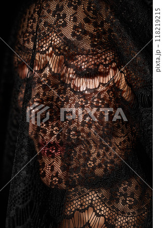 Close up of woman with eyes closed wearing black mourning veil made of delicate lace covering face in studio 118219215