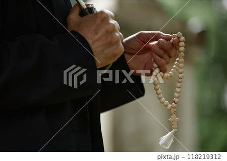 Close up on hands of unrecognizable senior person holding wooden rosary beads praying for soul of deceased at gravesite while hiding from rain under umbrella, copy space Close up on hands of unrecognizable senior person holding wooden rosary beads praying for soul of deceased at gravesite while hiding from rain under umbrella, copy space 118219312