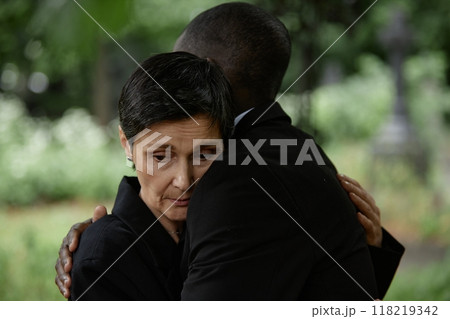 Portrait shot of sorrowful senior woman comforting husband with embrace grieving over loss of loved one during memorial ceremony at graveyard, copy space Portrait shot of sorrowful senior woman comforting husband with embrace grieving over loss of loved one during memorial ceremony at graveyard, copy space 118219342