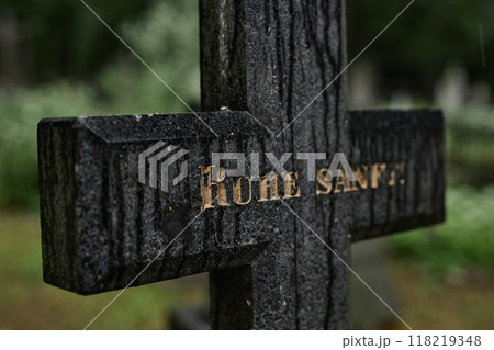 Background shot of granite memorial cross with engraved golden epitaph reads Ruhe Shaft standing in gloomy cemetery. Rain wet grave marker with traces of time commemorating passed away, copy space Background shot of granite memorial cross with engraved golden epitaph reads Ruhe Shaft standing in gloomy cemetery. Rain wet grave marker with traces of time commemorating passed away, copy space 118219348