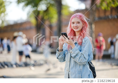 A girl with pink hair is holding a cell phone 118219618