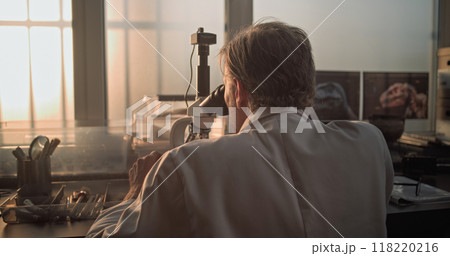Mature microbiologist analyzes fossil sample under microscope 118220216