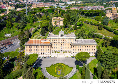 The Governorates Palace in Vatican is showcased from above, featuring its stunning architecture surrounded by meticulously manicured gardens and lush greenery, set against the city's backdrop. 118220573