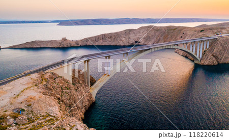 Pag Bridge with driving vehicles over Adriatic Sea channel at sunset. Road network connects island to Croatian mainland offering stunning views 118220614
