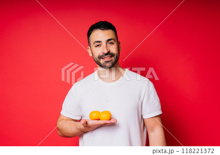 Handsome tall bearded white man with dark hair with tangerine on red background Handsome tall bearded white man with dark hair with tangerine on red background 118221372