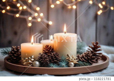 Burning Christmas candles with by pine branches and cones on a wooden table. 118221781