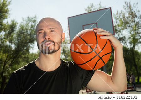 Happy basketball player holding basketball orange ball on shoulder on sports court. Basketball coach. Outdoors 118222132