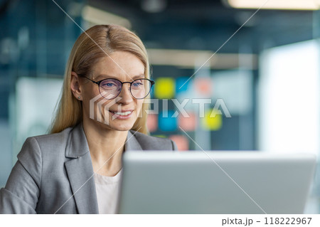 Businesswoman wearing glasses working on laptop in office. She appears confident and focused, surrounded by modern office interior. Professional attire suggests corporate environment Businesswoman wearing glasses working on laptop in office. She appears confident and focused, surrounded by modern office interior. Professional attire suggests corporate environment 118222967