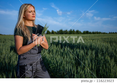 A female farmer standing in the wheat field, holding a tablet and wheat stalks A female farmer standing in the wheat field, holding a tablet and wheat stalks 118223023