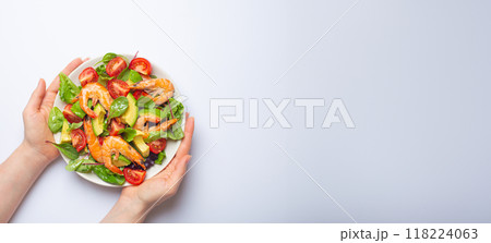 Female hands holding salad with grilled shrimps, avocado, vegetables, green leaves on white plate isolated on white background top view. Clean eating, nutrition and dieting concept, copy space. 118224063