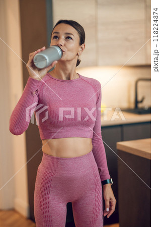 Fit woman dressed in sportswear drinking bottle of mineral water after her fitness training session 118224874