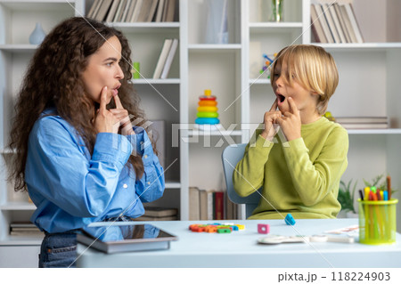 Blonde boy exercising with speech therapist and making efforts Blonde boy exercising with speech therapist and making efforts 118224903