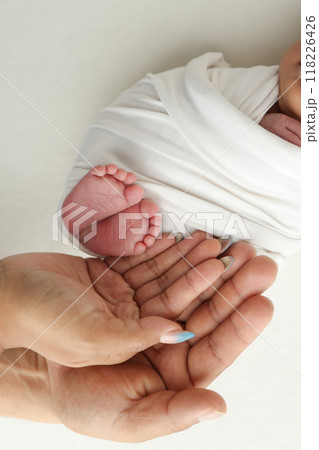 The palms of the parents. A father and mother hold the feet of a newborn child in a white blanket on a white background.. The feet of a newborn in the hands of parents. Photo of foot, heels and toes The palms of the parents. A father and mother hold the feet of a newborn child in a white blanket on a white background.. The feet of a newborn in the hands of parents. Photo of foot, heels and toes 118226426