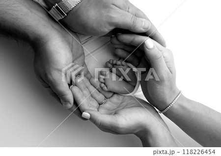 The palms of the parents. A father and mother hold the feet of a newborn child in a blanket. The feet of a newborn in the hands of parents. Black and white Photo of foot, heels and toes 118226454