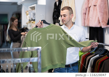 Man stopped near showcase with outerwear, holds blazer hanger in hands and examines product Man stopped near showcase with outerwear, holds blazer hanger in hands and examines product 118228047