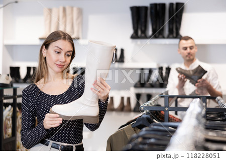Girl buyer looks at footwear from new collection and picks up new pair of high boot 118228051
